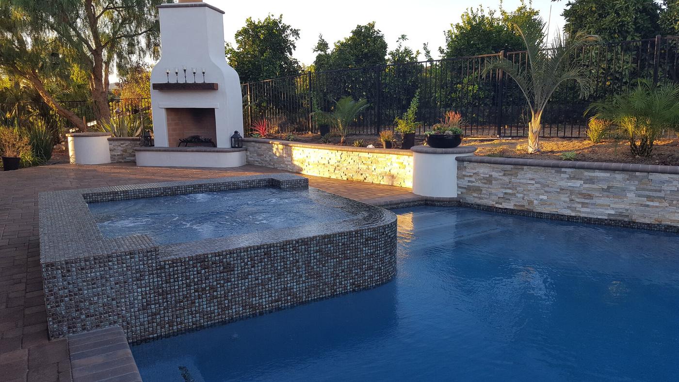 Raised spa with spillway and outdoor fireplace at dusk